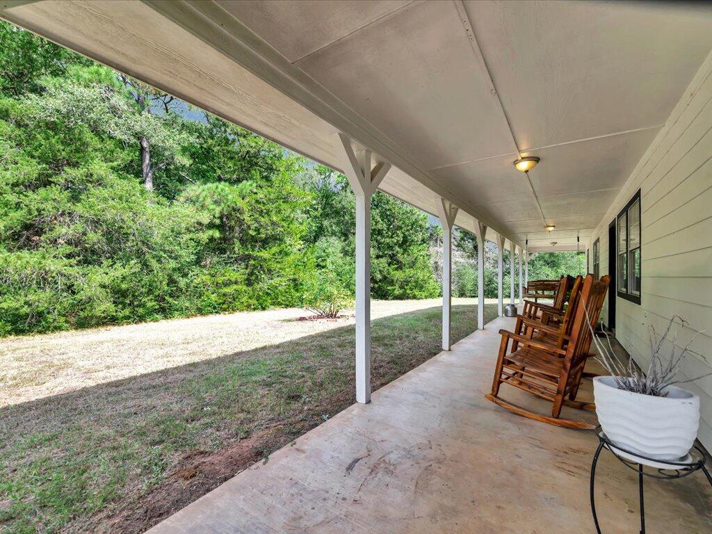 Covered porch with wooden rocking chairs overlooking a grassy yard and dense trees.