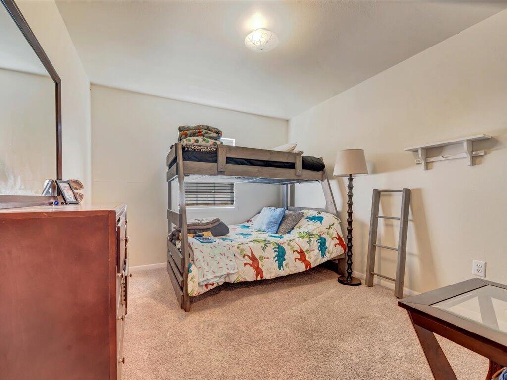 Bedroom with a wooden bunk bed, colorful bedding, beige carpet, and a dresser.