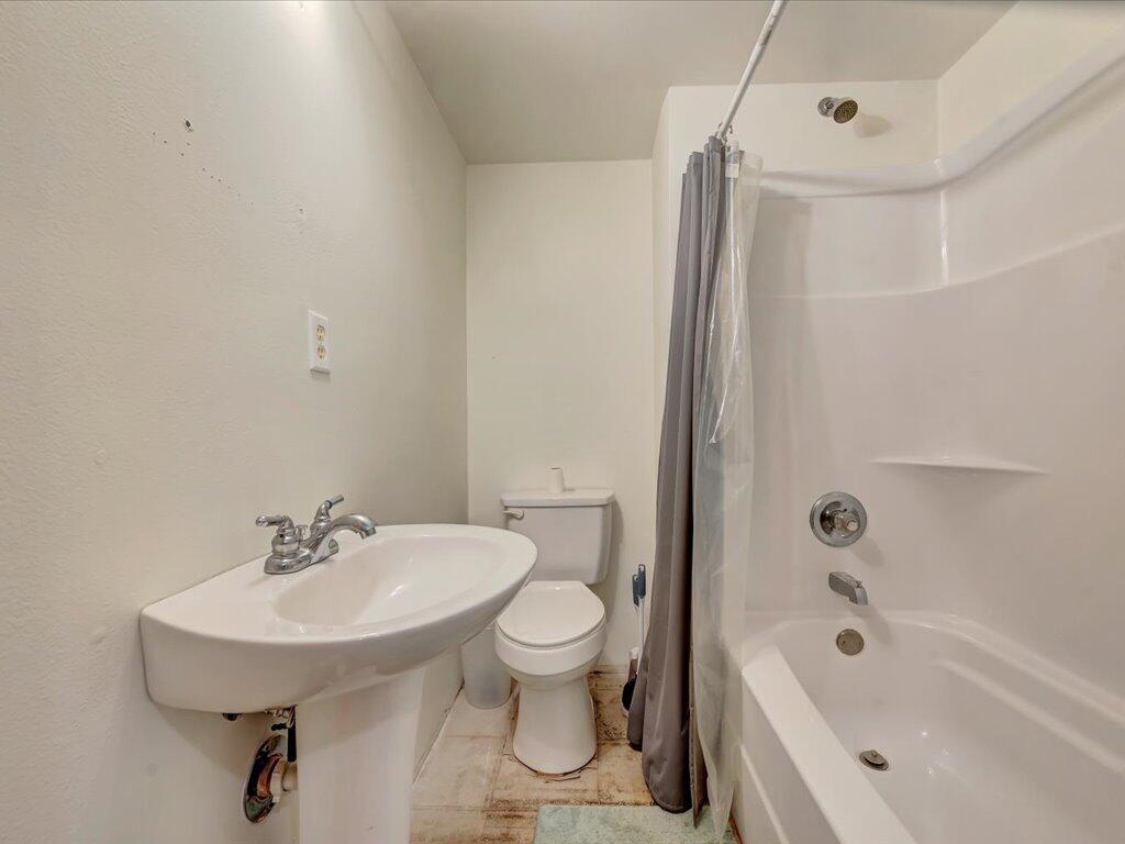 Bathroom with a pedestal sink, toilet, and bathtub behind a gray shower curtain.