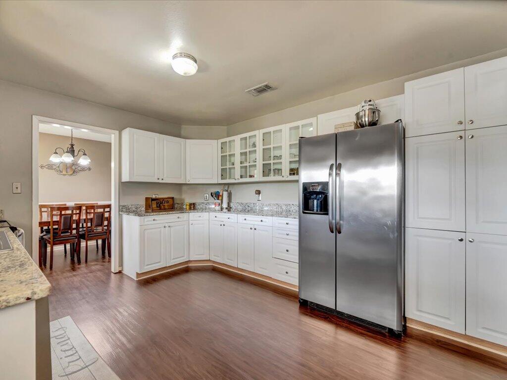 Kitchen with white cabinetry, granite counters, stainless steel refrigerator, and dark wood-look flooring.