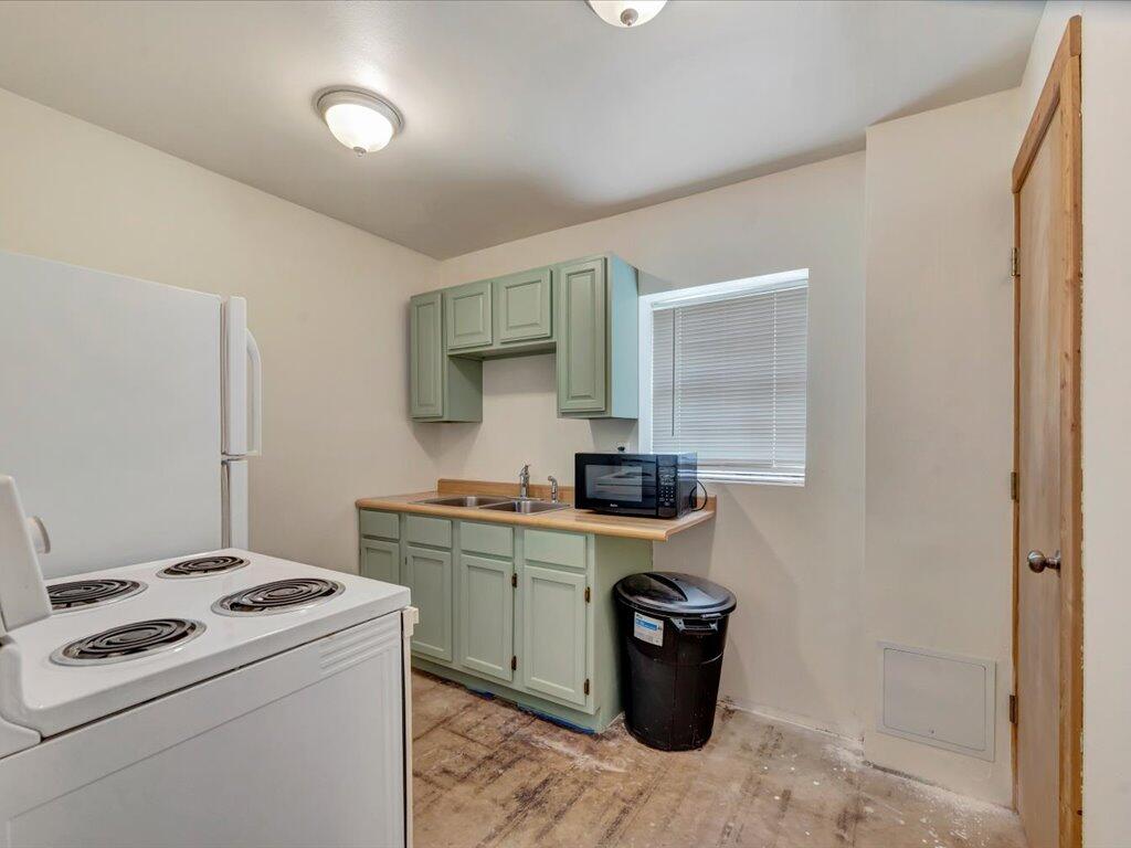 Compact kitchen with pale green cabinets, white appliances, and a microwave beside a window.
