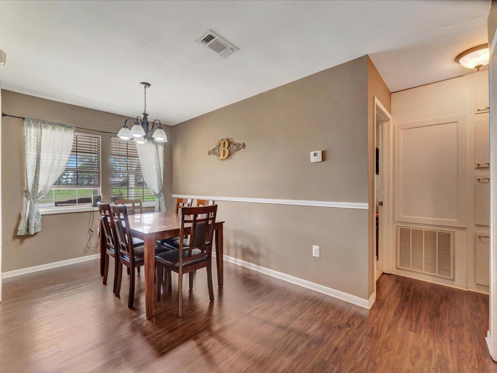 Dining room with a dark wood table beneath a chandelier and curtained windows overlooking a yard.