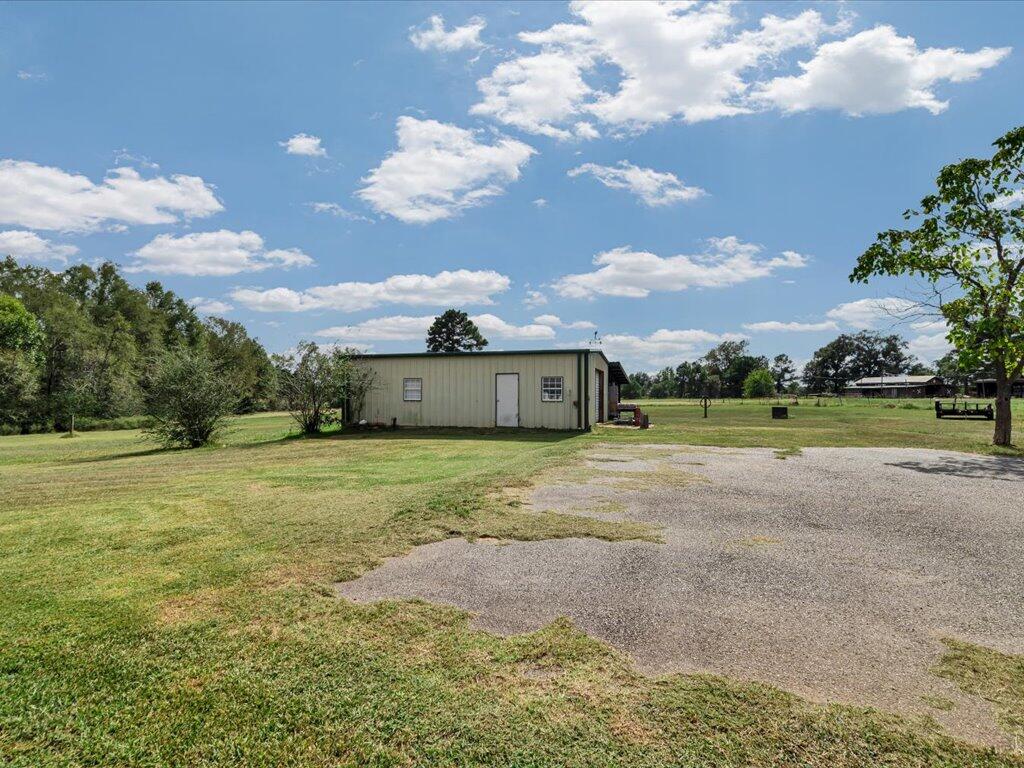 Small metal-sided building beside a gravel driveway on a spacious grassy lot.