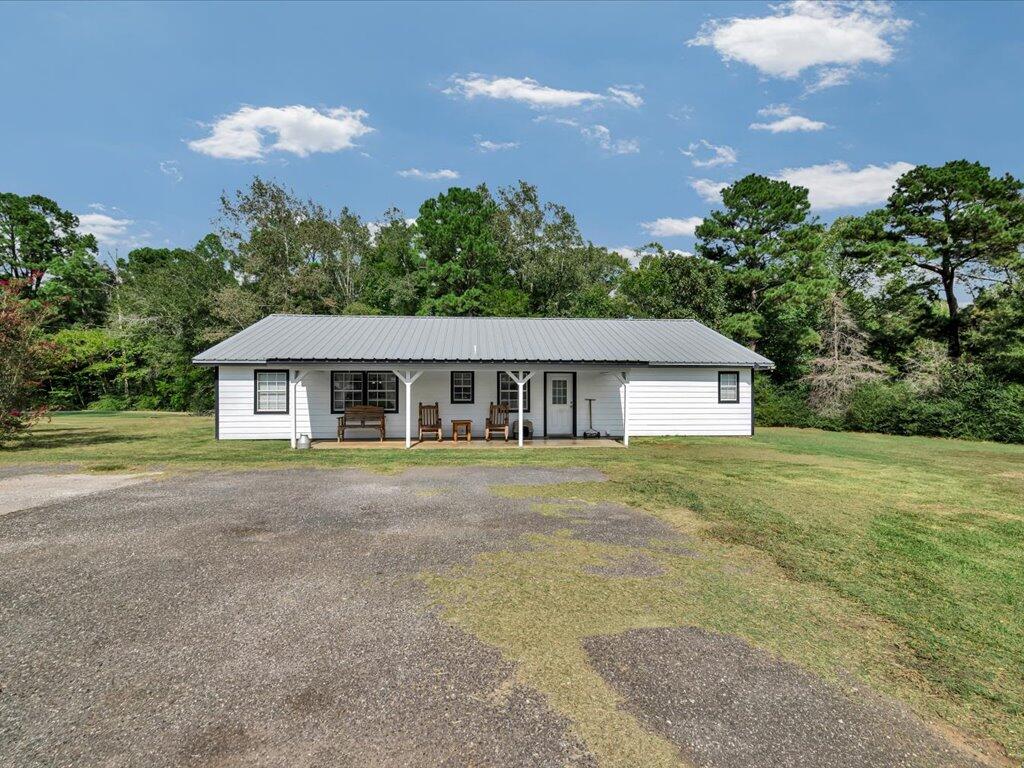 White single-story house with a metal roof, covered porch, and paved driveway.