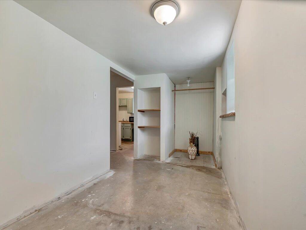 Hallway with a bare concrete floor, built-in shelves, and a doorway to the kitchen.