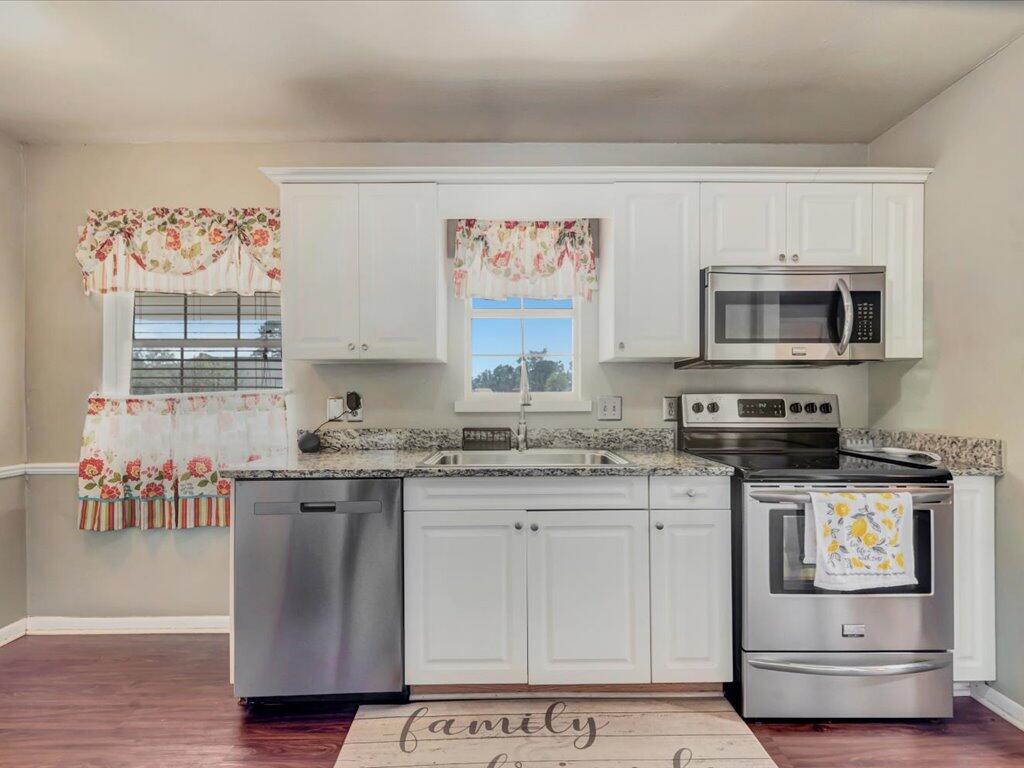 Kitchen with white cabinets, granite counters, stainless steel appliances, and floral curtains.