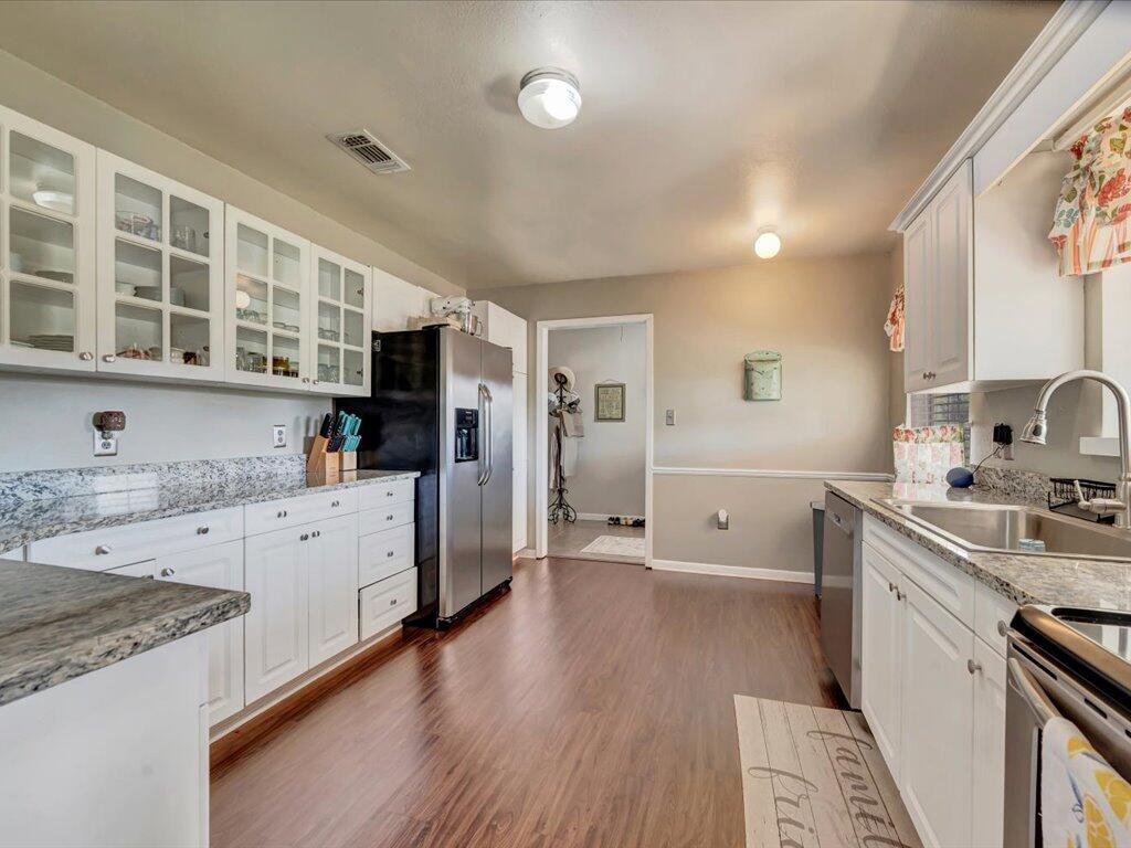 Kitchen with white glass-front cabinets, granite counters, stainless-steel appliances, and wood-look floors.