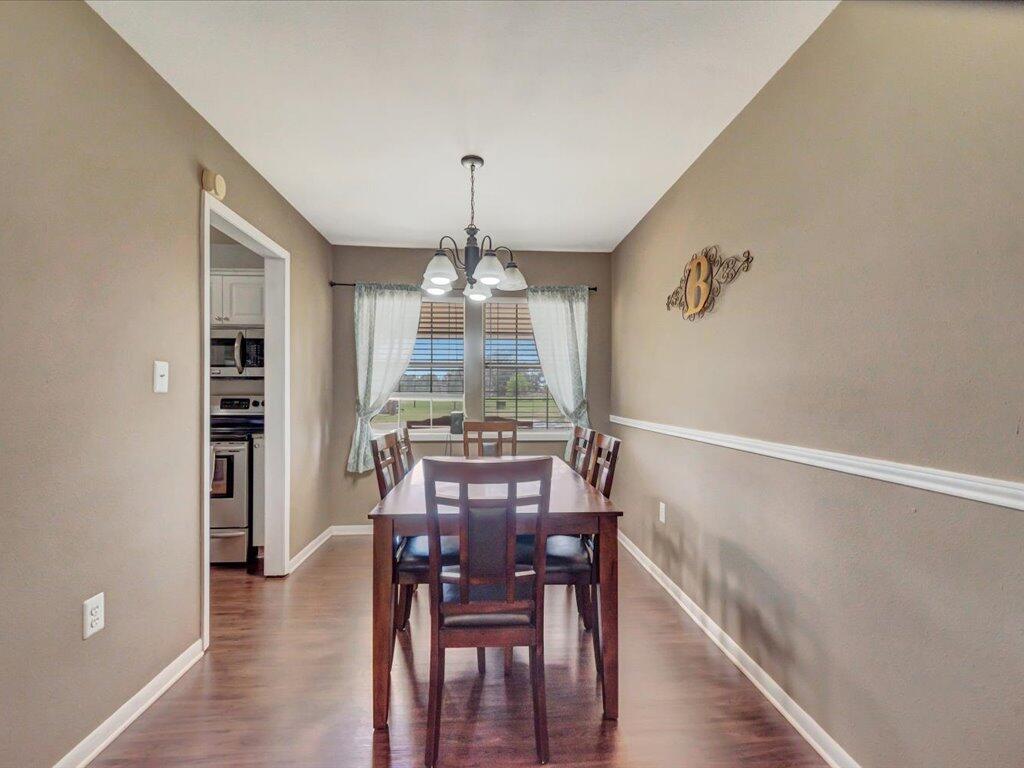 Dining room with a dark wood table and chairs beneath a chandelier, beside a window with curtains.