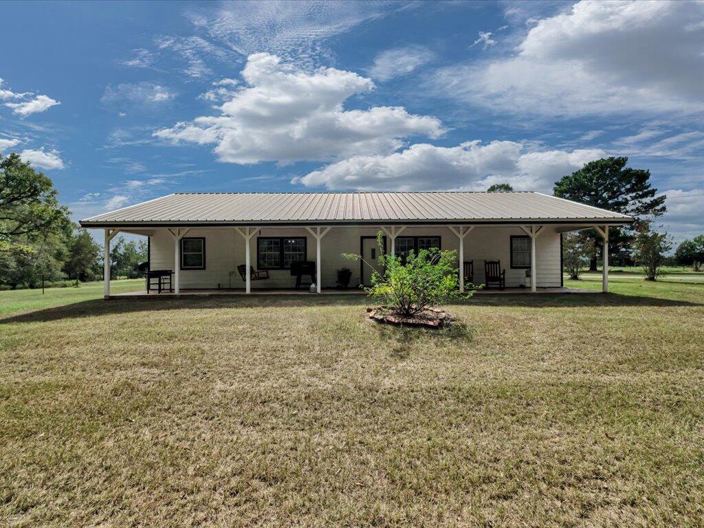 Single-story home with a long covered porch, metal roof, and open lawn.