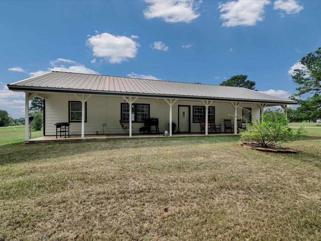 Single-story rural home with a long covered porch, metal roof, and grassy yard.