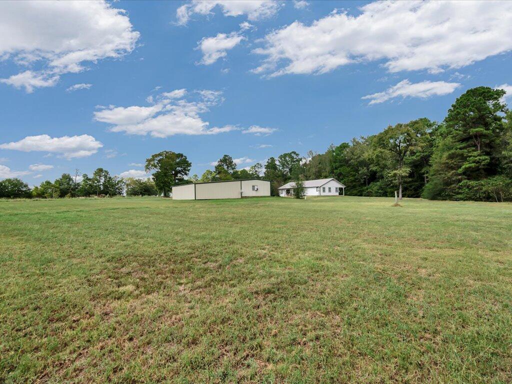 Grassy property with a white house and long metal outbuilding near the tree line.