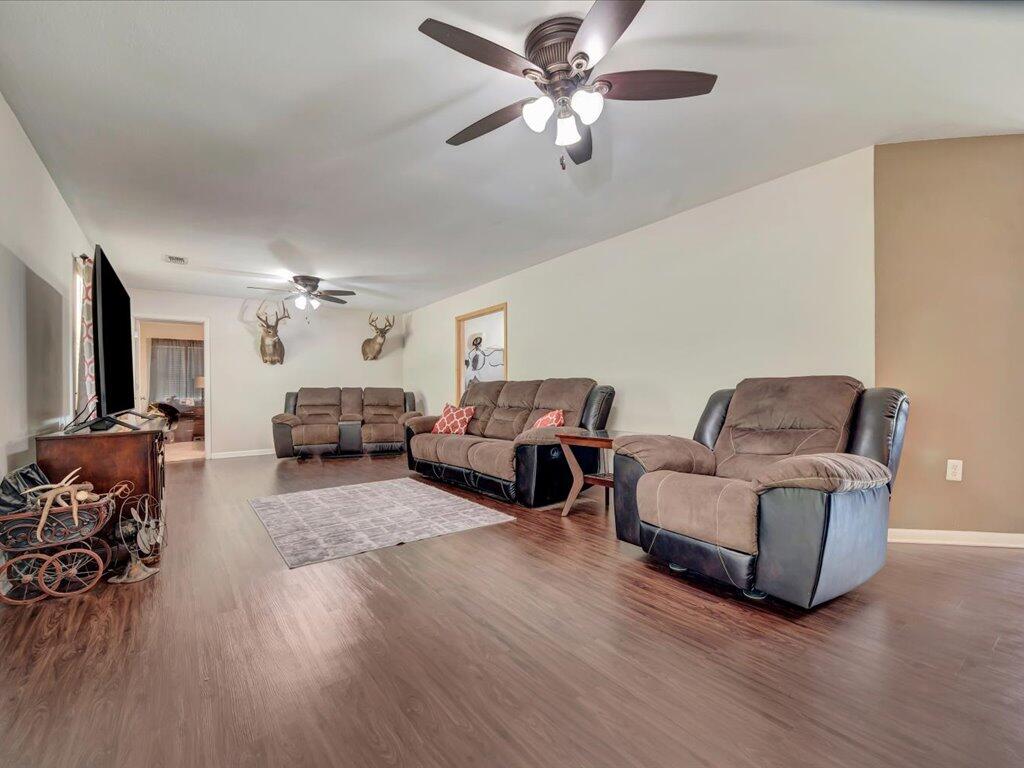 Living room with brown reclining furniture, two ceiling fans, and wood-look flooring.