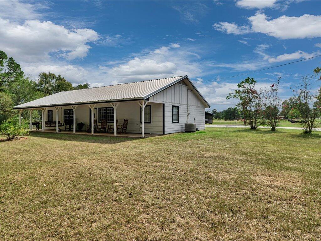 Single-story home with a covered porch, metal roof, and broad grassy yard.