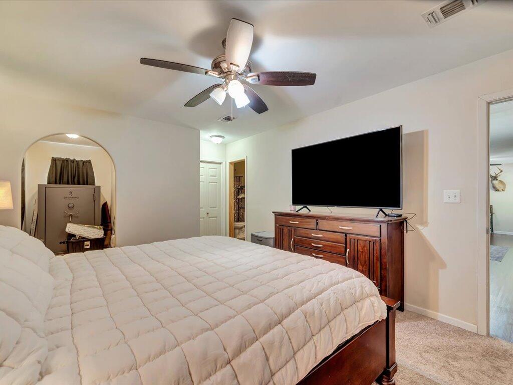 Bedroom with a large quilted bed, ceiling fan, and television on a wooden dresser.