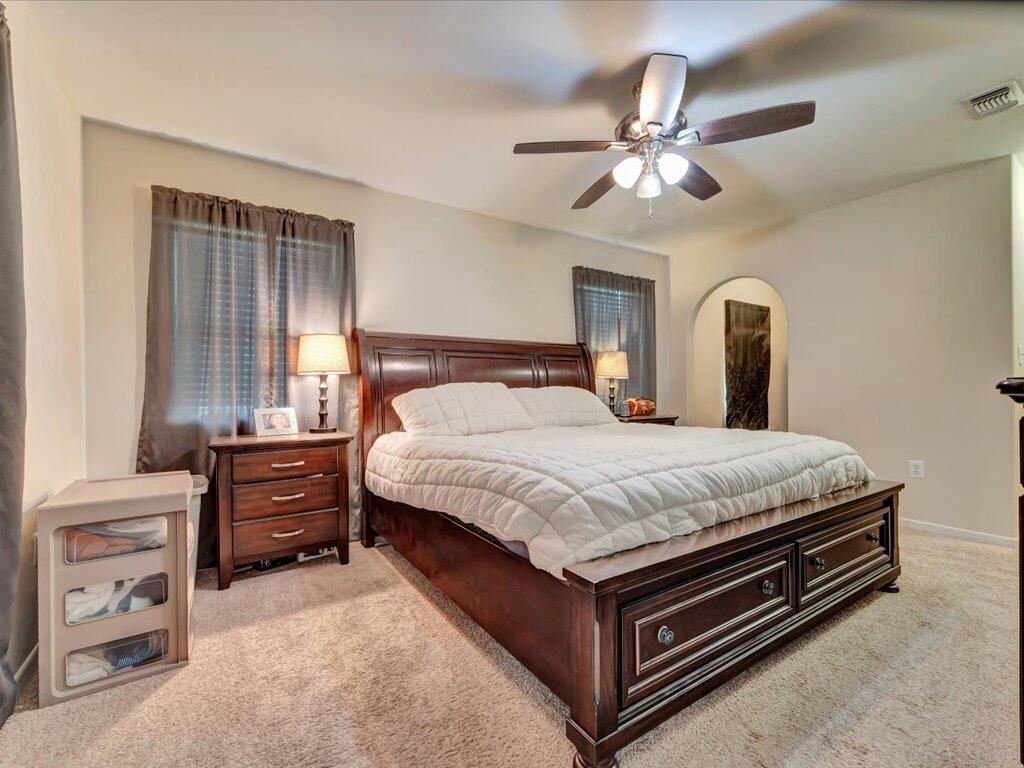 Furnished bedroom with a large dark wood bed, white quilt, curtained windows, and ceiling fan.