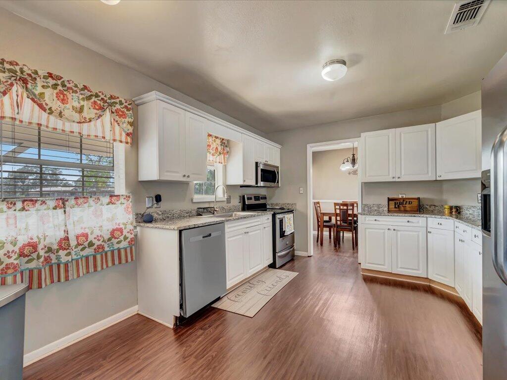 Kitchen with white cabinets, granite counters, stainless appliances, and floral window valances.