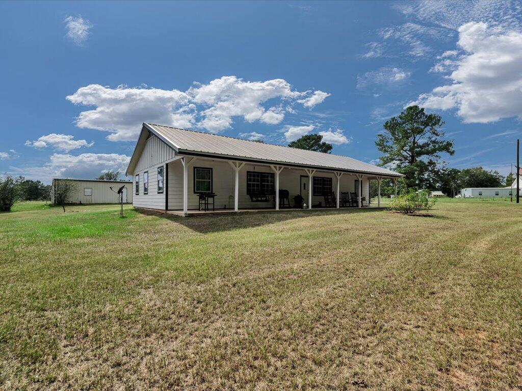 Single-story white house with a metal roof and covered porch on a broad grassy lot.