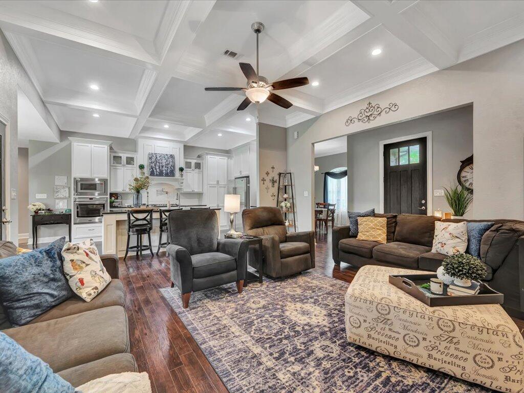 Open-plan living room and kitchen with a coffered ceiling, white cabinets, and dark wood floors.