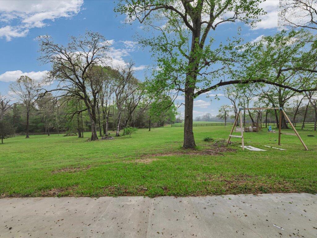 Grassy yard with mature trees and a wooden swing set beside a fence.