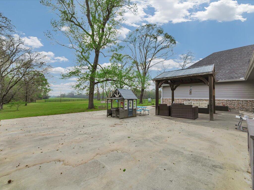 Concrete patio with a covered seating area and playhouse beside a tree-lined lawn.