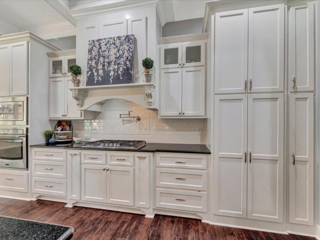 Kitchen with white cabinetry, a gas cooktop, decorative range hood, and dark countertops.