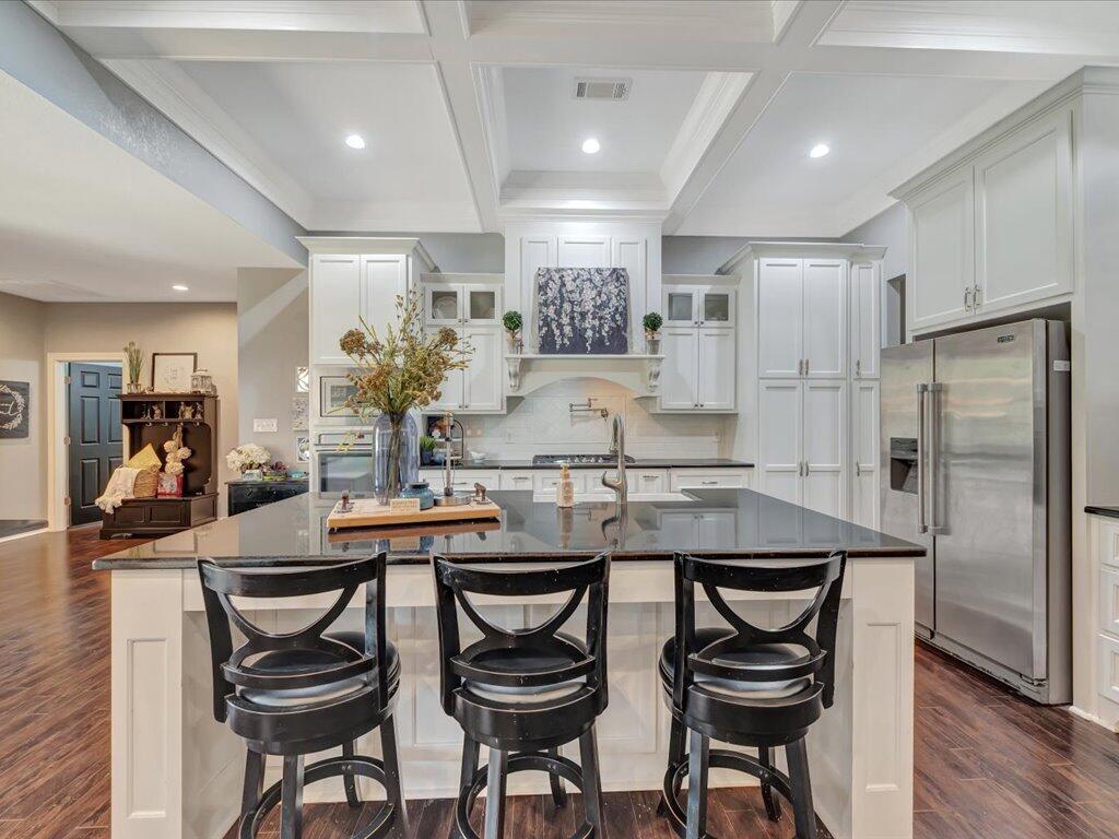 Kitchen with a dark island, three black bar stools, white cabinetry, and stainless steel appliances.
