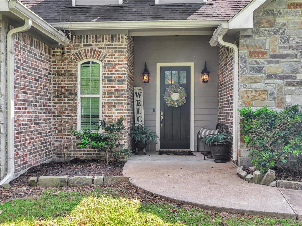 Covered home entrance with a dark wreath-adorned door, brick and stone walls, and an arched window.