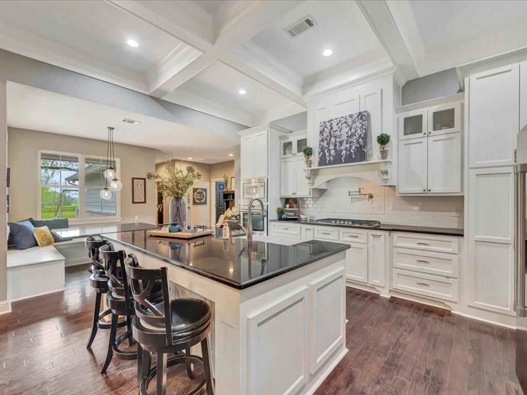 Bright kitchen with a large dark island, bar seating, white cabinetry, and a coffered ceiling.