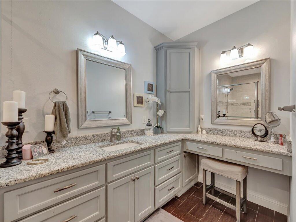 Bathroom vanity with gray cabinetry, granite counters, and two framed mirrors.