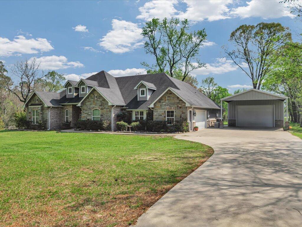 Stone-and-brick house with multiple gables, detached garage, broad lawn, and curved driveway.