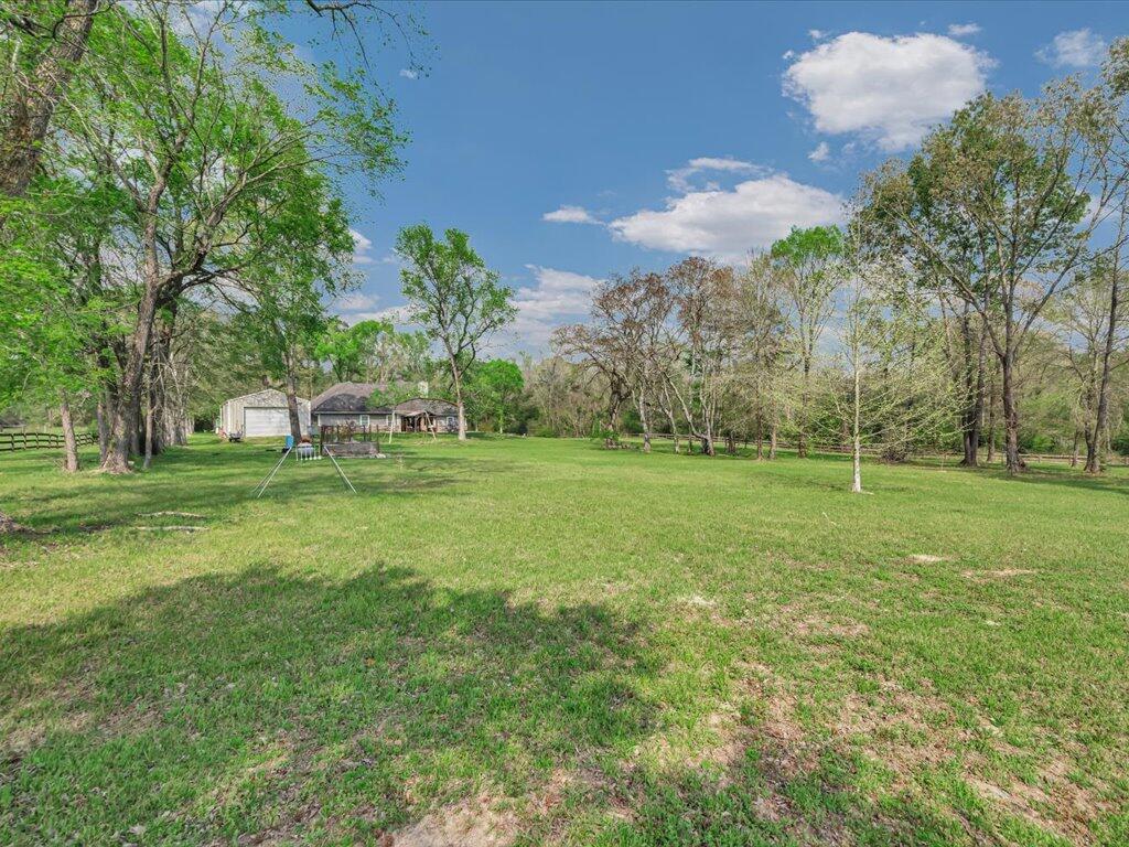 Expansive grassy yard with mature trees, distant outbuildings, and a swing set.