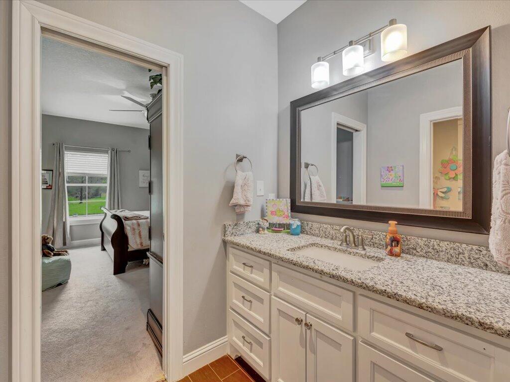 Bathroom vanity with granite countertop, white cabinets, and a large dark-framed mirror.