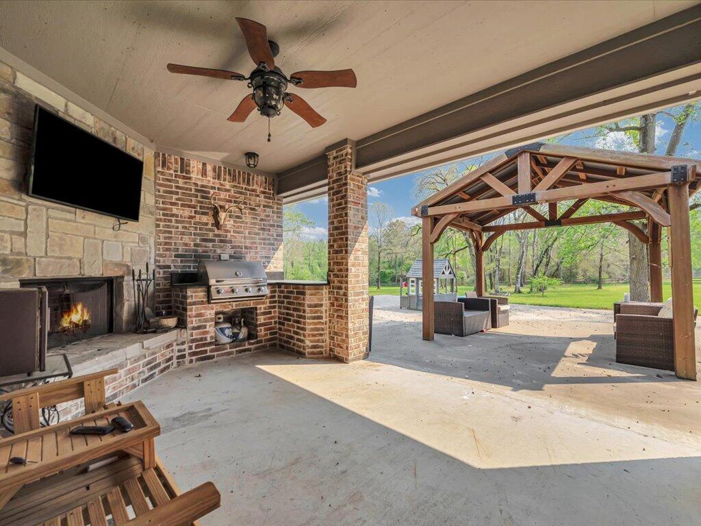 Covered patio with a stone fireplace and grill, opening to a yard with a wooden pergola.