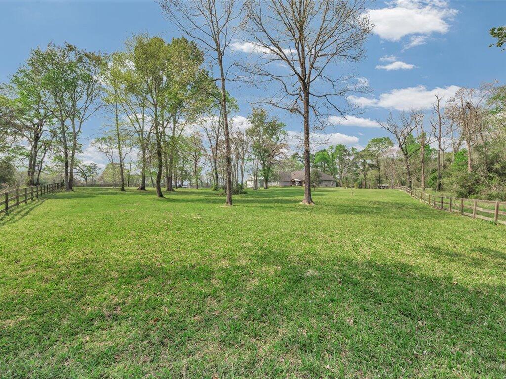Grassy yard with mature trees and split-rail fences, with a house in the distance.