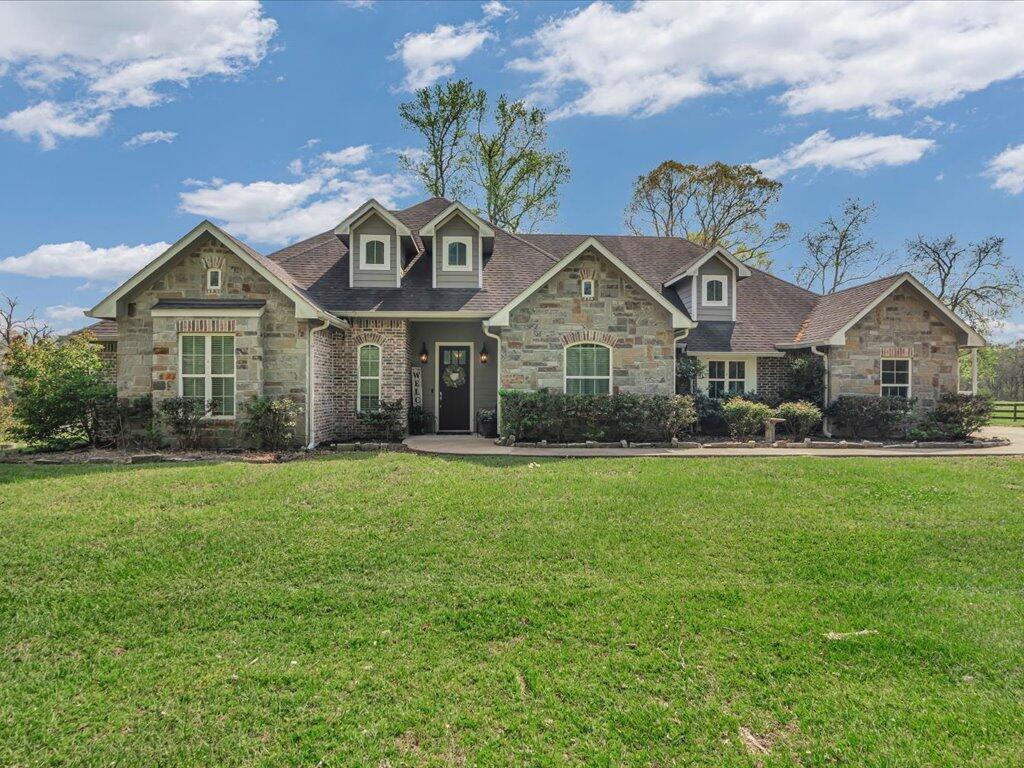 Stone-and-brick home with a multigabled roof and broad green lawn.