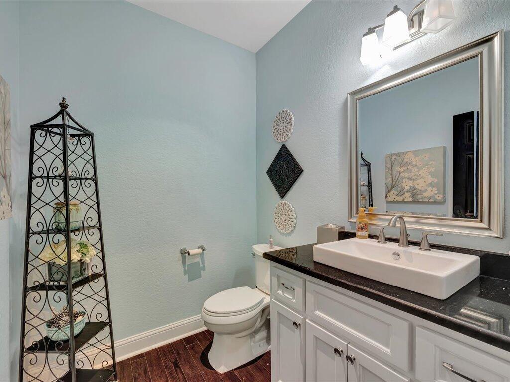 Bathroom with pale blue walls, white vessel sink, large framed mirror, and dark wood flooring.
