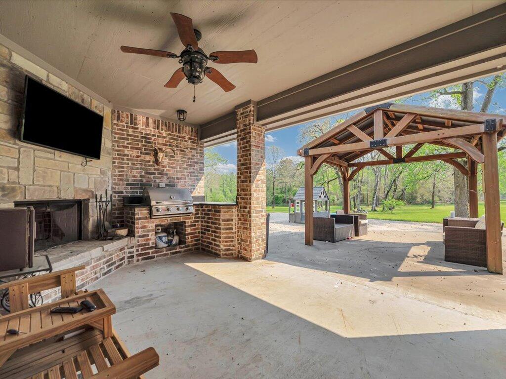 Covered patio with brick fireplace and grill, opening onto a pergola and tree-lined lawn.