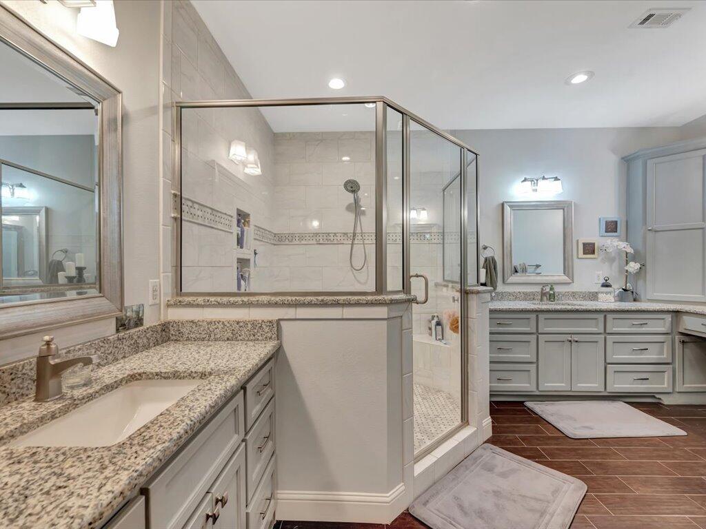 Bathroom with a glass-enclosed walk-in shower, granite counters, gray cabinetry, and dark tile flooring.