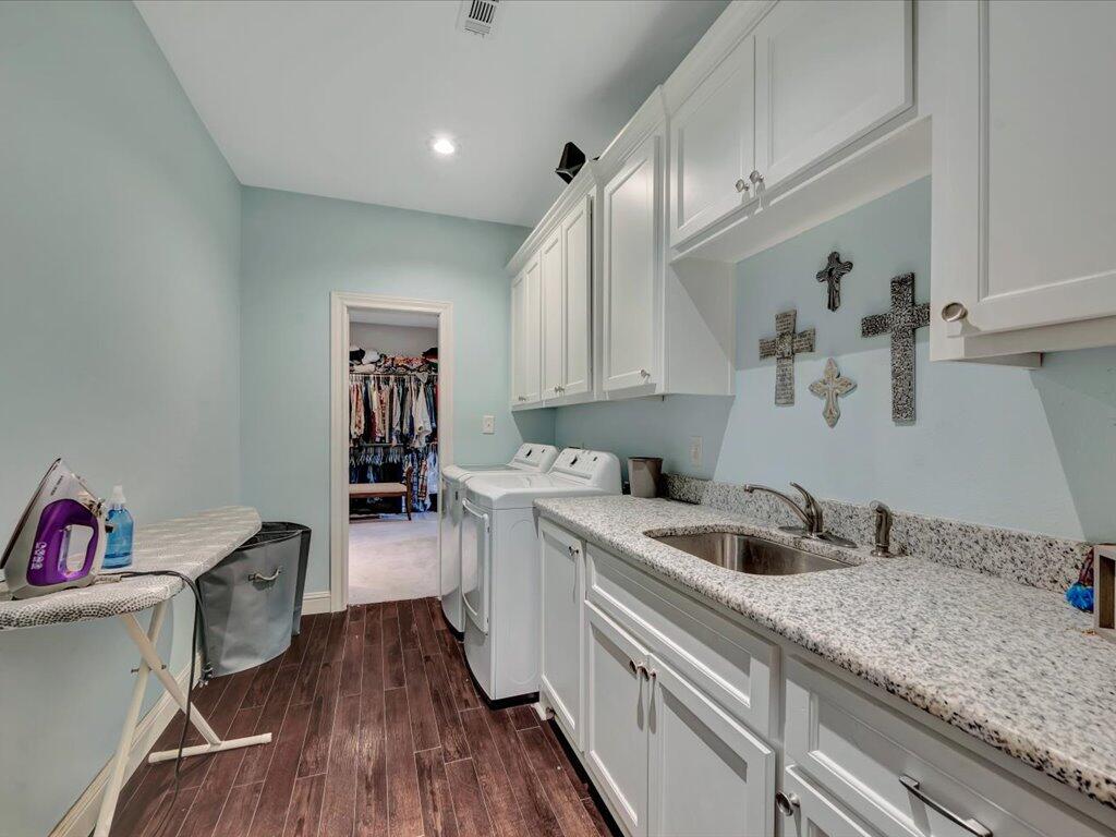 Laundry room with white cabinets, granite counter and sink, washer and dryer, and ironing board.