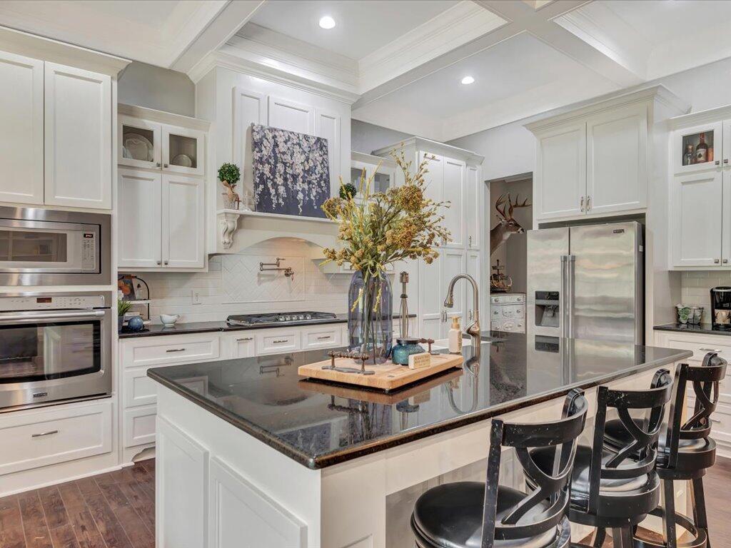 White kitchen with a large dark stone island, bar stools, and stainless steel appliances.