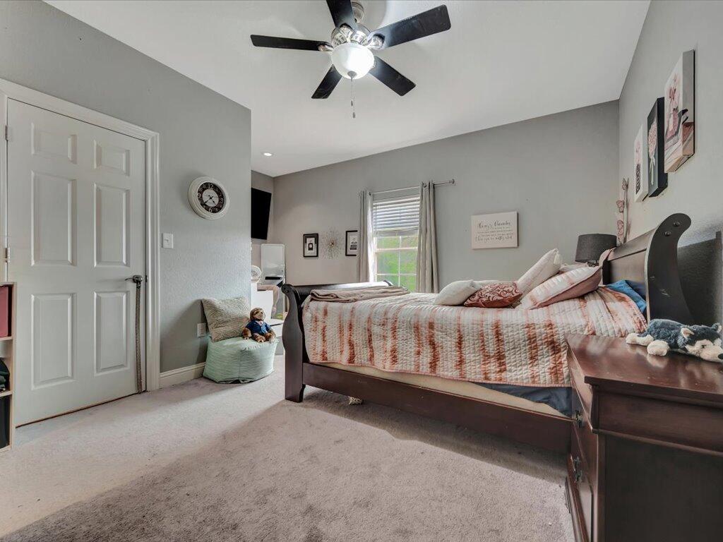 Furnished bedroom with a large striped-quilt bed, ceiling fan, and curtained window.