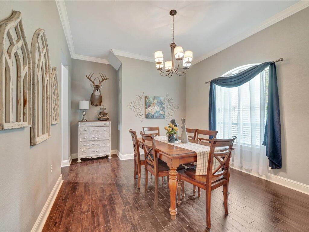 Dining room with a wooden table, chandelier, dark wood floors, and a large arched window with blue curtains.