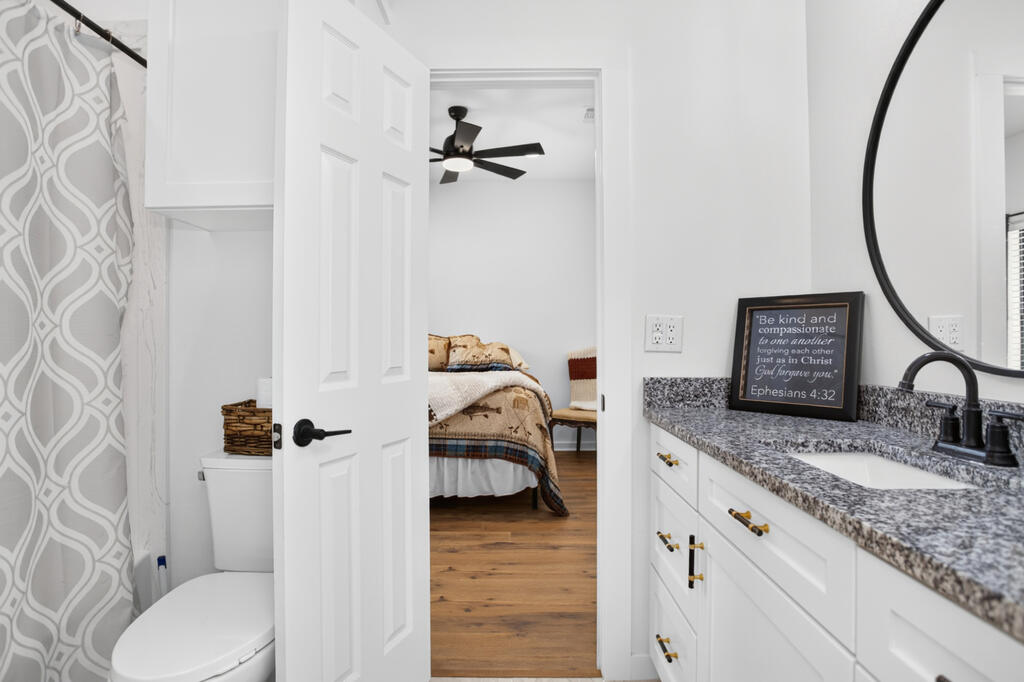 Bathroom with a granite vanity and black fixtures, opening onto a furnished bedroom.