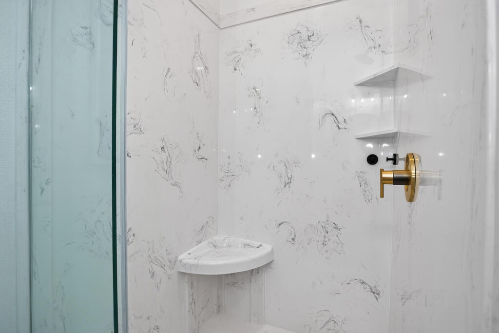 Walk-in shower with marble-look walls, a built-in corner seat, glass enclosure, and gold fixtures.