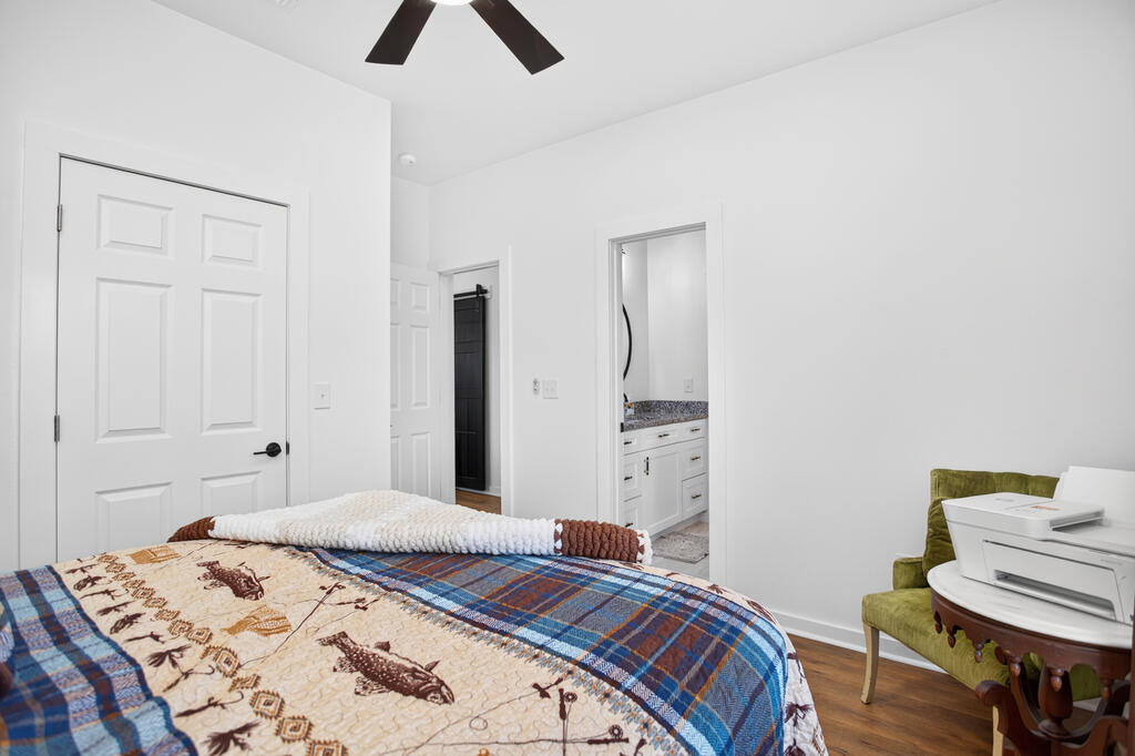 Bedroom with a patterned quilt, dark ceiling fan, and open doorway to a bathroom vanity.