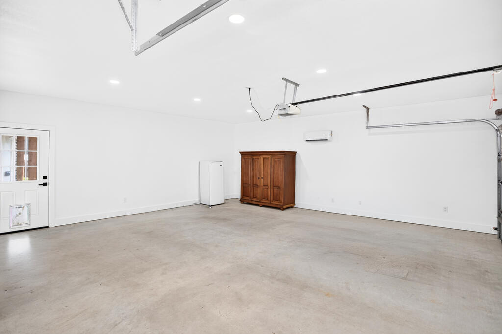 Spacious garage with a concrete floor, overhead door tracks, and wooden storage cabinet.