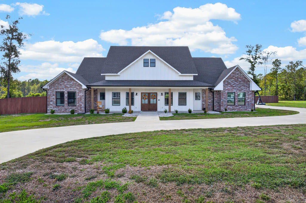 Home with brick wings, white siding, a covered porch, and a curved concrete driveway.