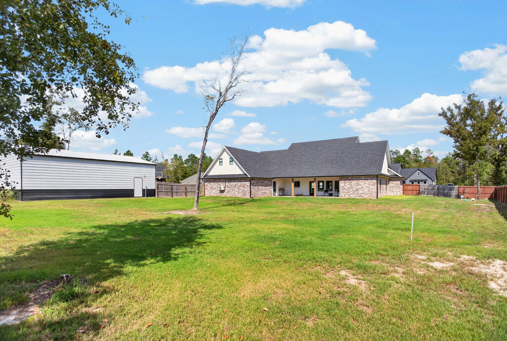 Single-story brick house beyond a broad grassy yard, with a detached metal-sided outbuilding to the left.