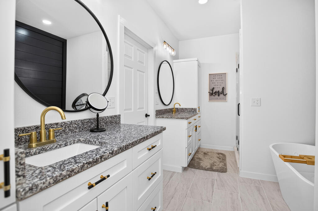 Bathroom with white vanities, speckled stone counters, gold fixtures, and a freestanding tub.