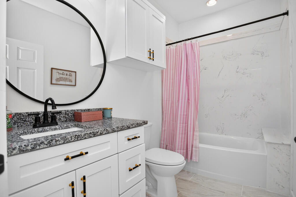 Bathroom with speckled vanity, round mirror, and tub behind a pink striped shower curtain.